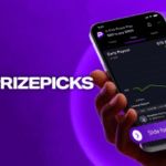 PrizePicks anuncia novo recurso de saída antecipada. Uma mão segura um smartphone exibindo o aplicativo PrizePicks com uma tela de Pagamento Antecipado mostrando um gráfico de pagamento crescente. O fundo é roxo com o logotipo e texto do PrizePicks no lado esquerdo.