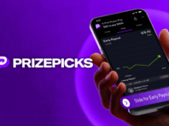 PrizePicks anuncia novo recurso de saída antecipada PrizePicks anuncia novo recurso de saída antecipada. Uma mão segura um smartphone exibindo o aplicativo PrizePicks com uma tela de Pagamento Antecipado mostrando um gráfico de pagamento crescente. O fundo é roxo com o logotipo e texto do PrizePicks no lado esquerdo.