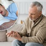 visão recortada de um homem idoso com doença de Parkinson segurando uma bengala enquanto está sentado no sofá em casa, imagem de stock