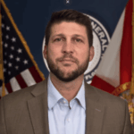 O procurador-geral da Flórida quer o aumento das penalidades para jogos de azar ilegais. O procurador-geral James Uthmeier, de blazer marrom e camisa clara, fica em frente às bandeiras dos EUA e da Flórida