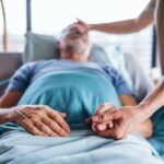 Uma mulher asiática madura enrolada em um cobertor, segurando uma xícara de café e olhando pela janela em profunda reflexão.