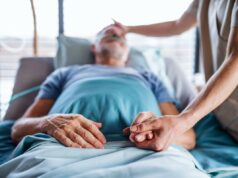 Querida Abby: Meu irmão está morrendo de ELA, mas a esposa dele não me deixa ficar na casa deles Uma mulher asiática madura enrolada em um cobertor, segurando uma xícara de café e olhando pela janela em profunda reflexão.