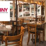 Área de jantar externa de um restaurante de Nova York instalada em uma calçada com mesas vazias e divisórias transparentes.