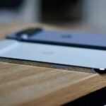 Um grande ícone do Quick Share centralizado em um fundo verde claro, com caminhos curvos pontilhados conectando mascotes do Android, pastas de documentos e ícones de dispositivos como telefone, tablet e laptop.