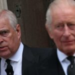 O príncipe André com o rei Carlos III desfocados ao fundo.