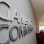 A Comissão de Jogos do Reino Unido discorre sobre as futuras mudanças de reforma no iGB Live 2025. Sinal da Comissão de Jogos do Reino Unido dentro do edifício. Reino Unido suspende licença da Deadheat Racing em meio a preocupações de responsabilidade social e AML