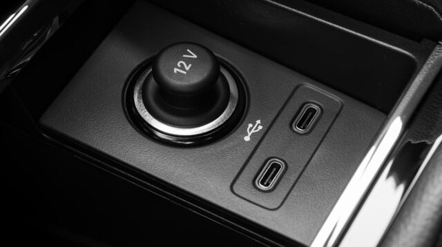 uma pessoa em um carro conectando um cabo USB-C a um smartphone com indicação de bateria fraca