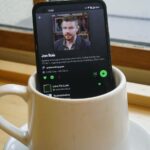 Logotipo do Spotify usando fones de ouvido pretos, cercado por ícones flutuantes de notas musicais verdes em um fundo gradiente.