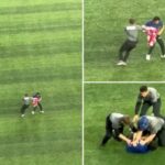 Segurança perseguindo um torcedor com bandeira canadense em campo.