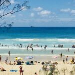 Seascape horizontal de pessoas aproveitando o sol de verão em férias turísticas na praia com areia turquesa ondas céu azul no famoso oceano de surf Byron Bay Austrália