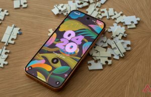 Os aplicativos Android que usei para controlar minha tela de bloqueio Mascote do Android entre caixas de papelão etiquetadas para aplicativos, capturas de tela, notificações e distrações, em frente à tela de um smartphone, com uma vassoura apoiada nas caixas.