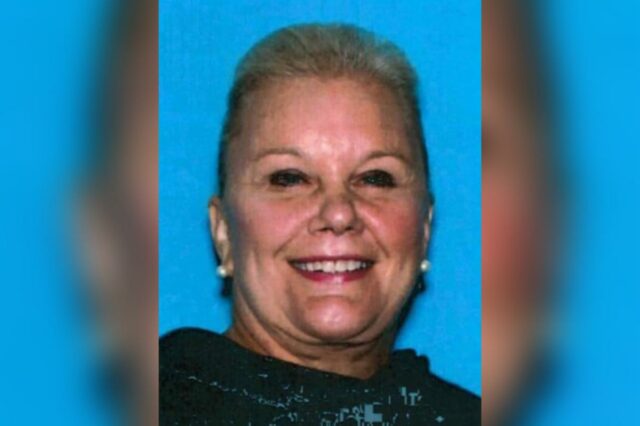 A falsa herdeira de uma companhia aérea, de 72 anos, Mugshot de uma mulher sorridente com cabelos claros em um top preto contra um fundo azul.