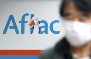 A gigante de seguros dos EUA Aflac diz que hackers roubaram dados pessoais e de saúde de 22,6 milhões aflac's logo in the background, with someone wearing a mask in the foreground.