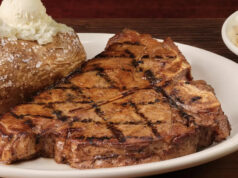 A rede de churrascarias que domina as vendas na América não é LongHorn ou Outback Logotipo do Texas Roadhouse no telefone com gráfico ascendente em segundo plano