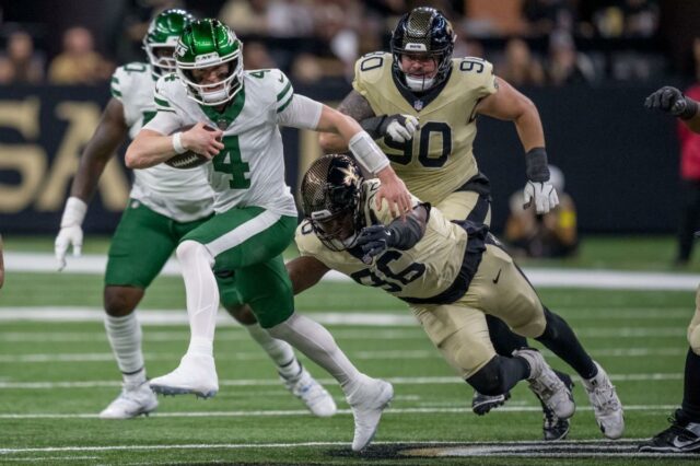 Aaron Glenn nunca considerou a mudança do Jets QB, apesar O quarterback do New York Jets, Brady Cook (4), corre com a bola enquanto o lado defensivo do New Orleans Saints, Carl Granderson (96), enfrenta outro jogador do Saints no primeiro tempo de um jogo de futebol.
