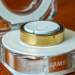 Um Samsung Galaxy Ring dourado apoiado verticalmente na borda de uma mesa de madeira