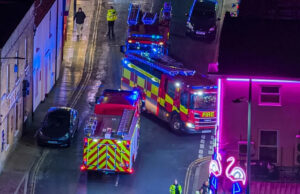Cenário pega fogo durante show de Natal A vista aérea da entrada do Hipódromo de Great Yarmouth mostra um grupo de pessoas conversando, incluindo pelo menos um bombeiro.