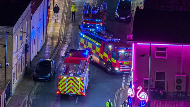 A vista aérea da entrada do Hipódromo de Great Yarmouth mostra um grupo de pessoas conversando, incluindo pelo menos um bombeiro.