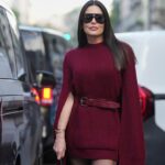 Diane Batoukina usa um pulôver de lã vermelho com padrão de Natal bordado branco, shorts pregueados de lã / tweed branco, anéis, uma bolsa de couro acolchoado vermelho brilhante pregado / cravejado da Valentino, durante uma sessão de fotos de moda de estilo de rua, em 15 de dezembro de 2021 em Paris, França.