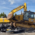 A Comissão de Controle de Jogos da Flórida destrói 147 caça-níqueis ilegais. Uma escavadeira CAT amarela passa e esmaga uma grande pilha de eletrônicos quebrados e detritos de metal em um terreno de concreto. Atrás dela, uma escavadeira Komatsu amarela está estacionada perto de uma área arborizada sob um céu azul.