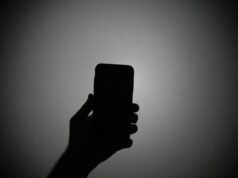 Conheça a equipe que investiga quando jornalistas e ativistas são invadidos por spyware do governo The silhouette of a hand holding an iPhone with the light on.