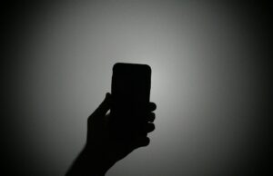 Conheça a equipe que investiga quando jornalistas e ativistas são invadidos por spyware do governo The silhouette of a hand holding an iPhone with the light on.