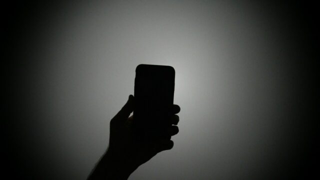 The silhouette of a hand holding an iPhone with the light on.