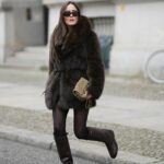 Um convidado usa óculos de sol circulares, um cardigã curto vermelho fofo de mangas curtas / abotoado, calça jeans azul marinho de pernas largas, uma bolsa cesta de vime marrom, um lenço de seda com estampa verde / azul / laranja, anéis, sapatos de salto de couro envernizado branco brilhante, um cinto de corrente de ouro, fora do desfile da Hermes, durante a Paris Fashion Week - Menswear Primavera/Verão 2023, em 25 de junho de 2022 em Paris, França.