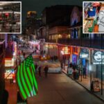 Bourbon Street à noite com pedestres, letreiros de néon e uma bandeira americana iluminada em verde.