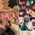 Mãos pintando um enfeite de massa salgada em formato de galo de laranja e branco, cercado por outros enfeites coloridos de massa salgada e potes de tinta.