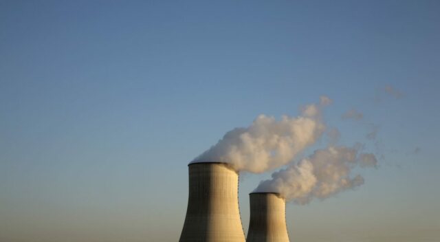 Cooling towers for a nuclear reactor stand against a blue sky.