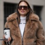 PARIS, FRANÇA - 11 DE DEZEMBRO: Alicia Aylies usa cabelo preso em um rabo de cavalo baixo e elegante, pele natural com sobrancelhas definidas e batom, um boné de beisebol preto NY, um top curto branco da Celine, um casaco longo de pele sintética marrom com corte reto e fecho de botão, jeans azul claro de cintura alta com perna larga e bainha crua e sapatos escuros de salto alto com bico pontudo, durante uma sessão de fotos de moda de estilo de rua, em 11 de dezembro, 2025 em Paris, França. (Foto de Edward Berthelot/Getty Images)