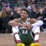 O jogador de basquete Giannis Antetokounmpo sentado na quadra durante um jogo.