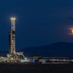 Fervo's drilling rig lit up at night with the moon rising in the background.