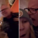 Max Towey de óculos de armação preta gritando com uma mulher de gorro.