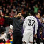 Kobbie Mainoo em pé com os braços na cintura pelo Manchester United.