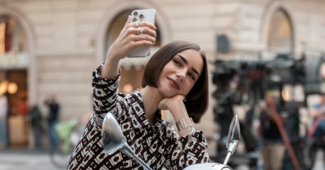 Lily Collins explica por que Emily tem um Bob na Emily tirando uma selfie. Na foto: Lily Collins.