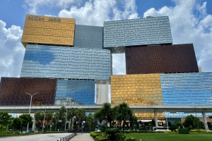 MGM Resorts estende acordo de marca à medida que a MGM China fortalece o desempenho de Macau. Moderno complexo resort MGM Cotai em Macau com design de torre empilhada de vidro e ouro, palmeiras em primeiro plano e céu azul acima.