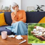 Uma mulher madura doente com um resfriado comum assoando o nariz com um lenço de papel enquanto está sentada em um sofá em casa.