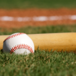 O memorando da MLB proíbe os jogadores de aderirem a contratos de previsão de eventos de mercado - relatório. Uma vista de perto de um taco de beisebol e de madeira descansando na grama verde perto da borda de uma linha de terra no campo.