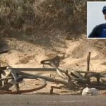 Detritos, incluindo uma bicicleta mutilada, no acostamento de uma estrada próxima a um banco de areia com mato seco.