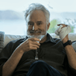 A man drinks from a glass and smiles