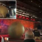 Uma grande bola cinza pairando no ar acima de um palco com uma pessoa visível.