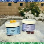 Agricultor segurando sementes de cânhamo nas mãos, com o sol poente e plantas de cânhamo ao fundo.