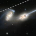 Uma imagem de duas galáxias em interação com um raio de luz no canto superior esquerdo.