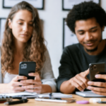 O mundo das apostas distorce os homens? Uma mulher e um homem estão sentados lado a lado em uma mesa, olhando para seus smartphones em cadernos abertos, sugerindo que estão comparando informações ou participando juntos de uma atividade on-line.