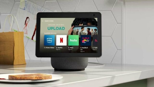 Um Echo Spot em uma mesa de cabeceira ao lado de uma luminária