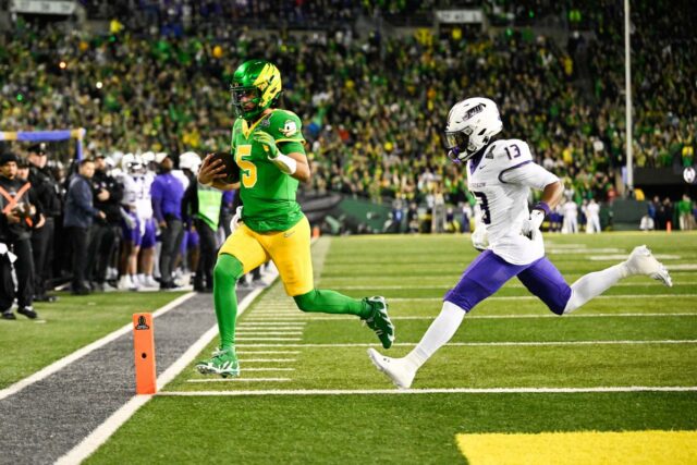 O quarterback do Oregon Ducks, Dante Moore (5), correndo para um touchdown enquanto o safety de James Madison Dukes, Tyler Brown (13), defende.
