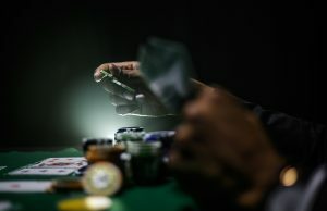 Os mercados de jogos de azar estão se tornando o entretenimento em primeiro lugar e as apostas em segundo? Pessoa segurando dinheiro sobre a mesa de pôquer com fichas e cartas de baralho com pouca luz. Os mercados de jogos de azar estão se tornando o entretenimento em primeiro lugar e as apostas em segundo?