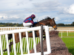Os números da Entain mostram que o Grand National foi mais uma vez o maior evento de apostas do ano Close-up de um jóquei em um cavalo saltando sobre um obstáculo de feno, paisagem rural ao fundo. Grand National lidera os eventos de apostas mais populares do mundo, mostram números da Entain